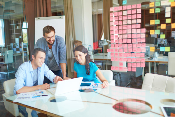 Group of business partners in casual listening to young man pointing at laptop screen in office